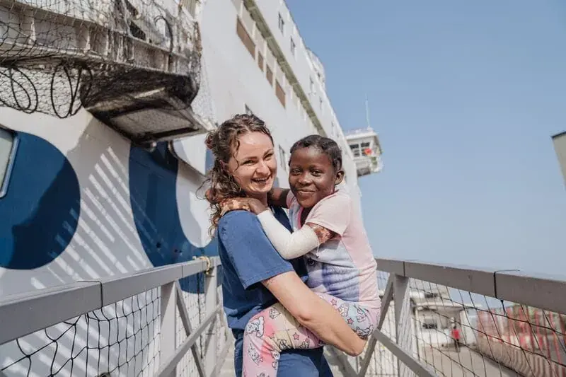 Een verpleegkundige zit naast een patiënt aan boord van een ziekenhuisschip.